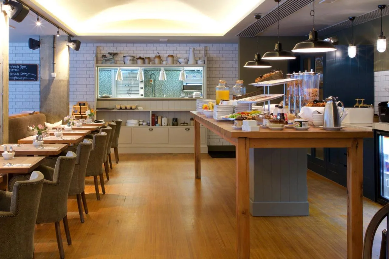 a restaurant with tables and chairs and a kitchen at Bermondsey Square Hotel - A Bespoke Hotel in London