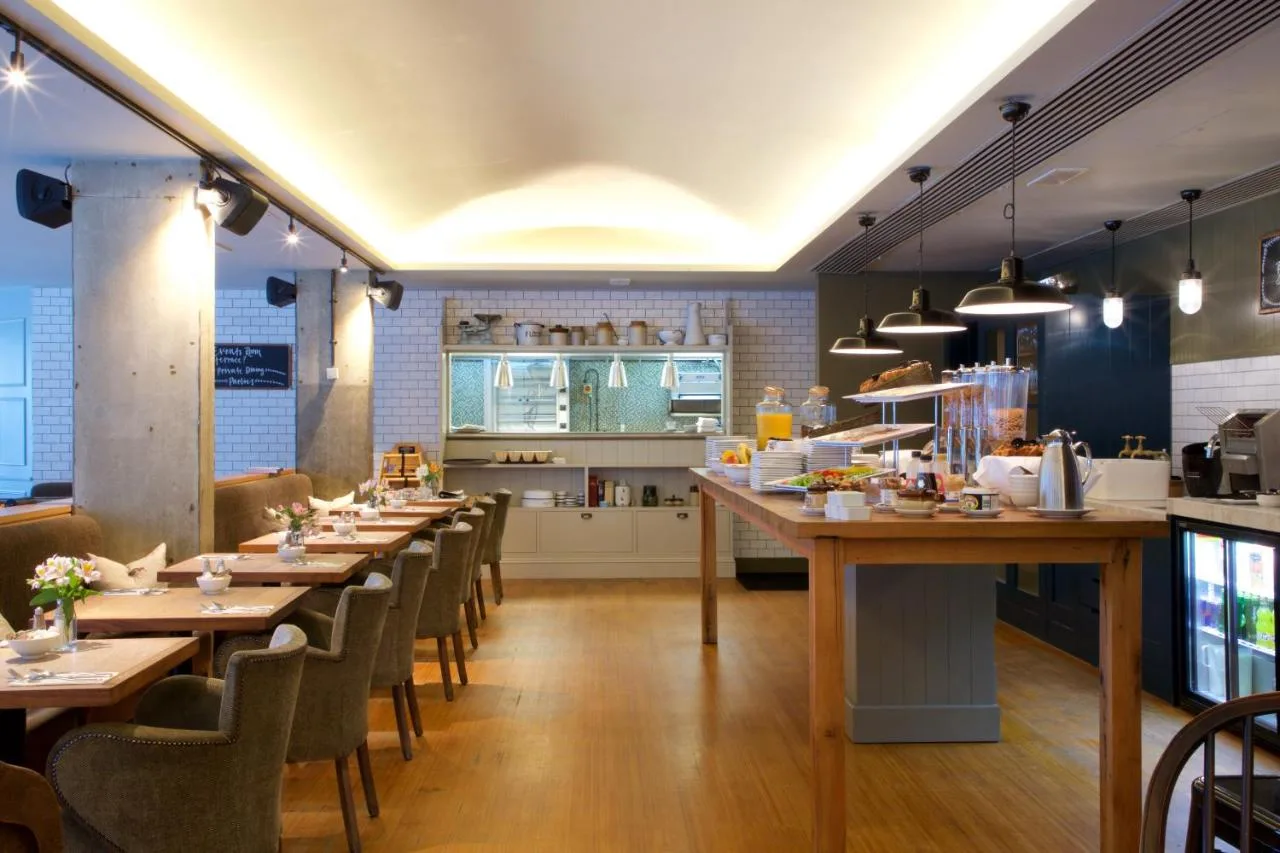 a restaurant with wooden tables and chairs and a kitchen at Bermondsey Square Hotel - A Bespoke Hotel in London